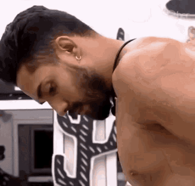 a shirtless man with a beard and earrings on his ears is looking down .