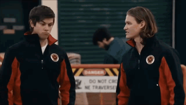 two men standing next to each other in front of a sign that says danger