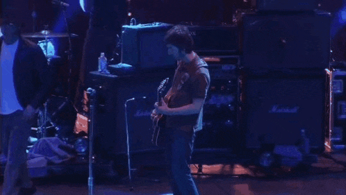 two men are playing guitars on a stage in front of a drum set .