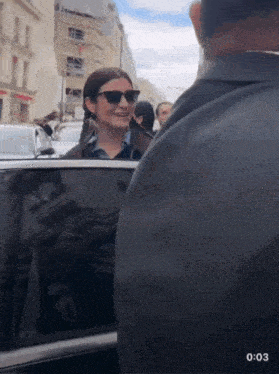 a woman wearing sunglasses is getting out of a car with the time of 0:03