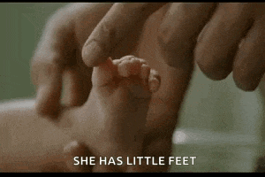 a person is touching a baby 's foot with their finger and says `` she has little feet '' .