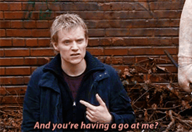 a man is pointing to his chest and says " and you 're having a go at me " in pink letters