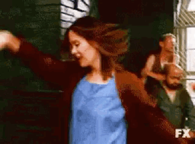a woman is dancing in front of a group of people in a room with the fx logo in the corner .