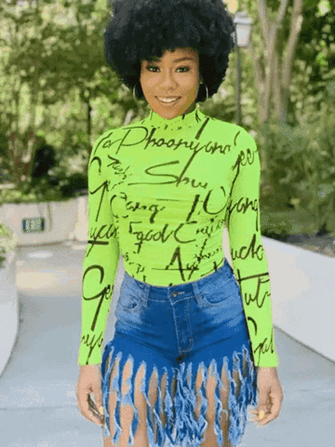 a woman wearing a neon green top and denim shorts with fringe