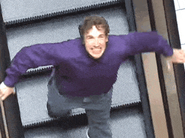 a man in a purple shirt is jumping up an escalator