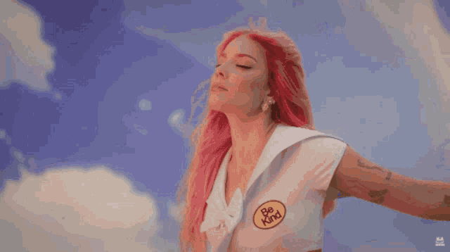 a woman with pink hair is wearing a be kind sticker on her shirt