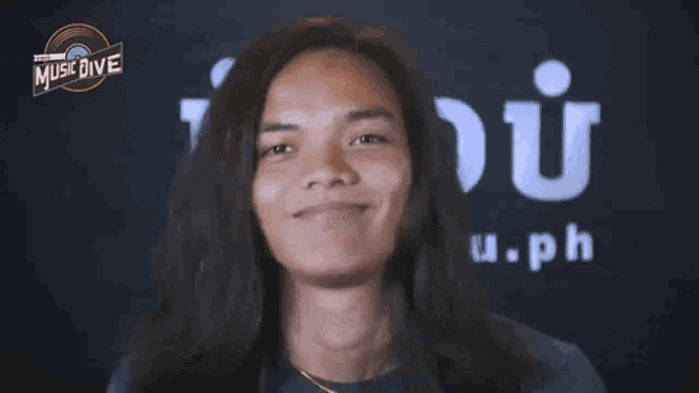 a young man with long hair is smiling in front of a sign that says music dive