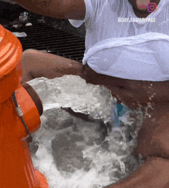 a man in a white shirt is sitting in a fire hydrant with water pouring out of it