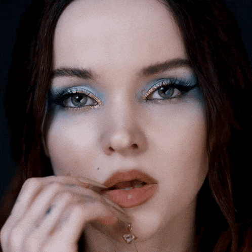 a close up of a woman 's face with blue eyeshadow and a necklace