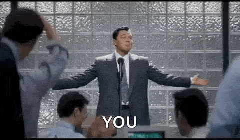 a man in a suit and tie is giving a speech in front of a group of people and says `` you '' .