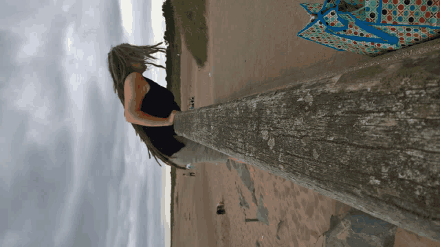 a woman leaning against a wooden post on a beach