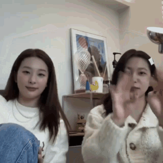 two women are sitting next to each other in a room with a picture on the wall