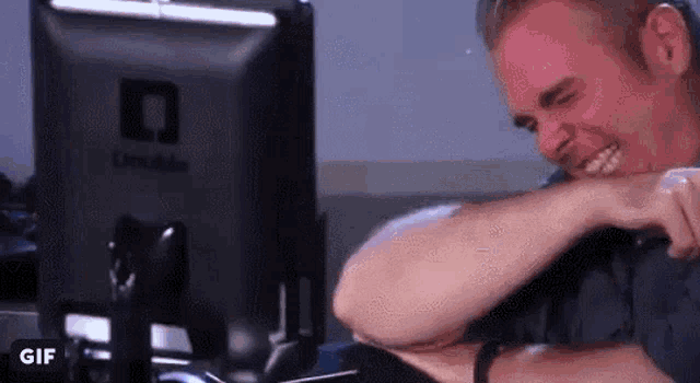a man is laughing while sitting in front of a computer screen .