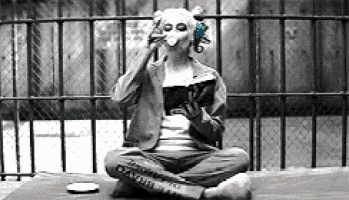 a person wearing a mask is sitting on the ground reading a book and drinking from a cup .