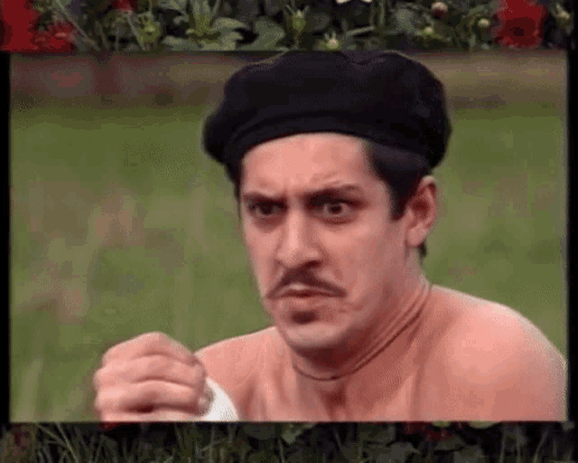 a shirtless man wearing a black beret and a mustache is making a face .