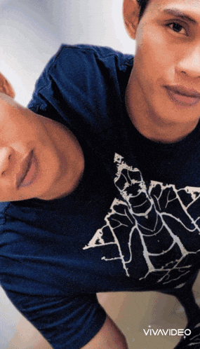a man wearing a blue shirt with a spider on it is standing next to another man