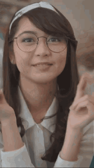 a young woman wearing glasses and a headband is smiling and giving a peace sign .
