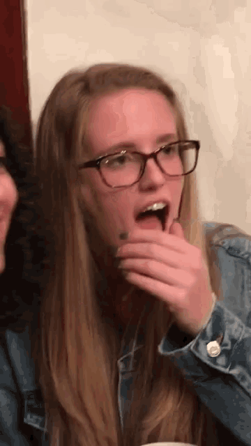 a girl wearing glasses is covering her mouth with her hands