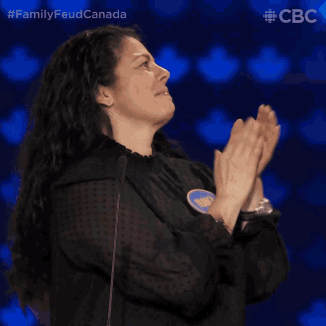 a woman applauds in front of a microphone with the hashtag #familyfeudcanada