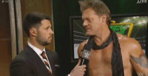 a man in a suit and tie is talking to a shirtless wrestler with a microphone .