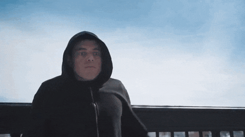 a man in a hooded jacket is sitting on a balcony looking at the sky .