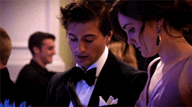 a man in a tuxedo and a woman in a purple dress are looking at something