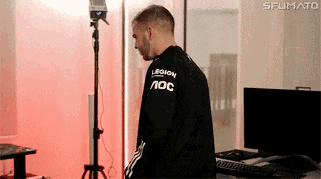 a man wearing a black shirt that says legion aoc is standing in front of a computer .