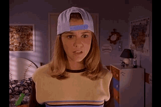 a young woman wearing a baseball cap and a striped shirt is standing in a bedroom .