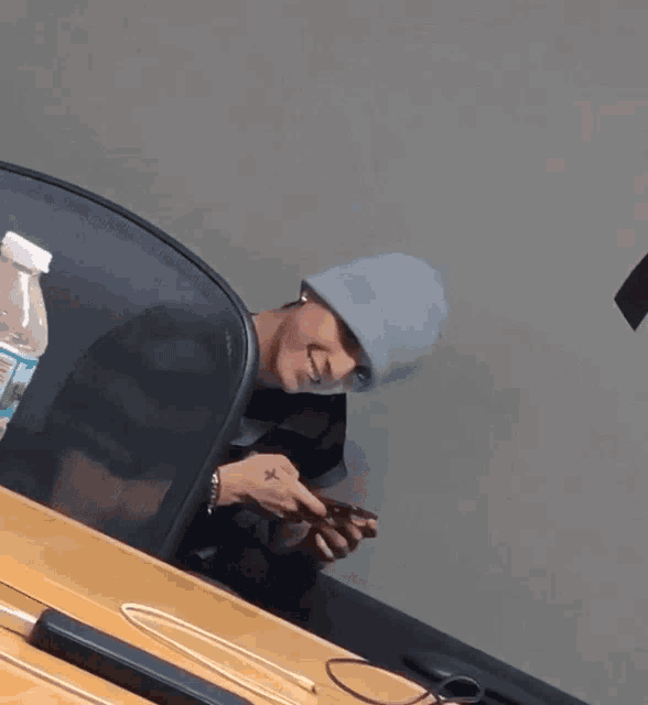 a man wearing a beanie is sitting at a desk looking at his cell phone