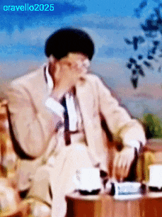 a man in a suit and tie is sitting at a table with a cup of coffee and a cigarette in his hand