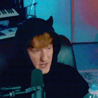 a man wearing a black cat ear hoodie is sitting in front of a microphone .