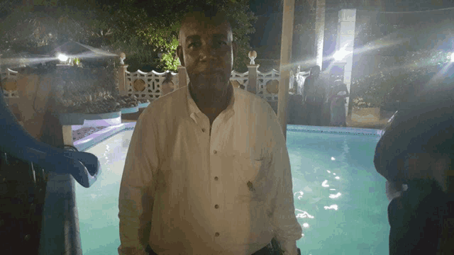 a man in a white shirt stands in front of a swimming pool at night