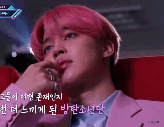 a man with pink hair is sitting in a chair with a sign that says next