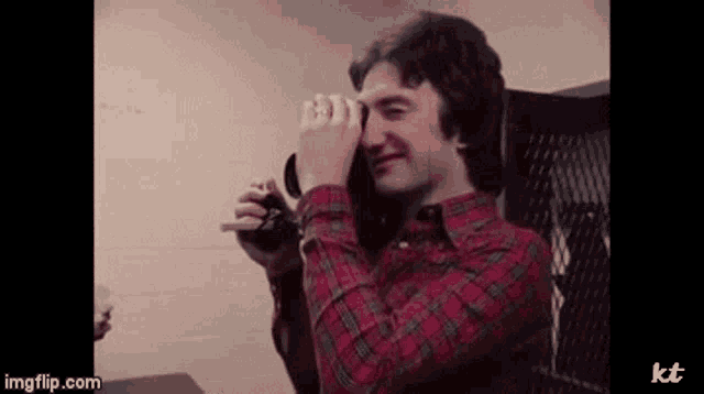 a man in a plaid shirt is holding a camera and taking a picture .