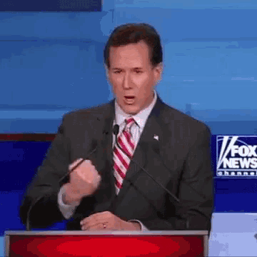 a man in a suit and tie is giving a speech in front of a fox news sign
