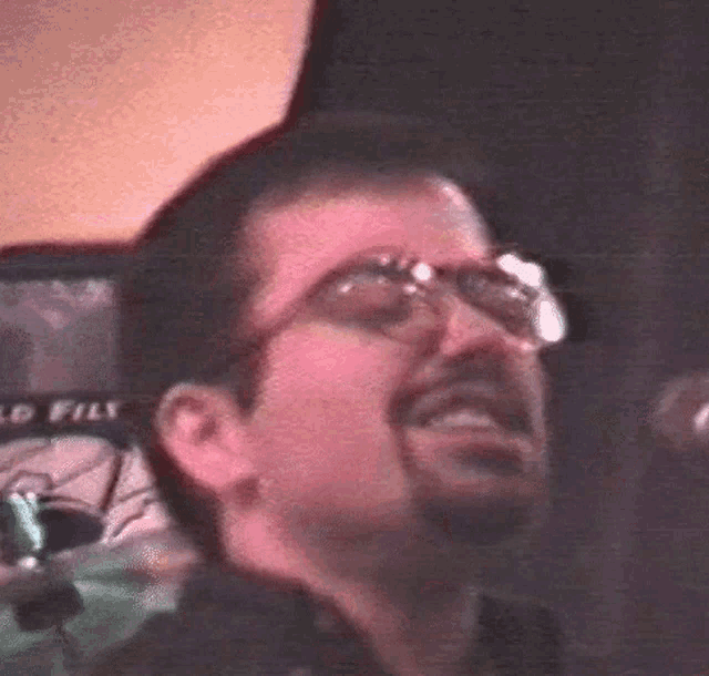 a man with glasses and a beard is smiling in front of a sign that says world files