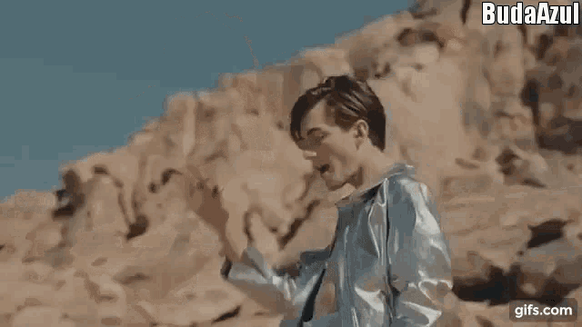 a man wearing a cowboy hat and leather jacket is standing in the desert .