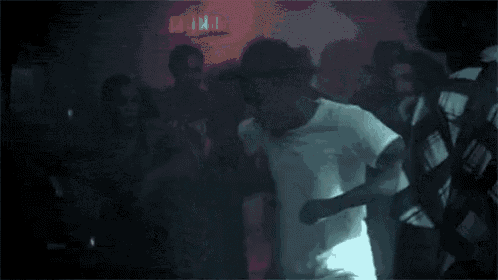 a man in a white shirt is dancing in a crowd of people in a club .