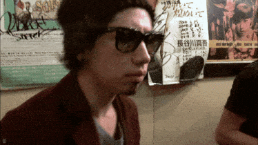 a man wearing sunglasses stands in front of a sign that says ' tokyo ' on it