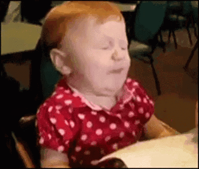 a baby is sitting in a high chair with his eyes closed and making a funny face .