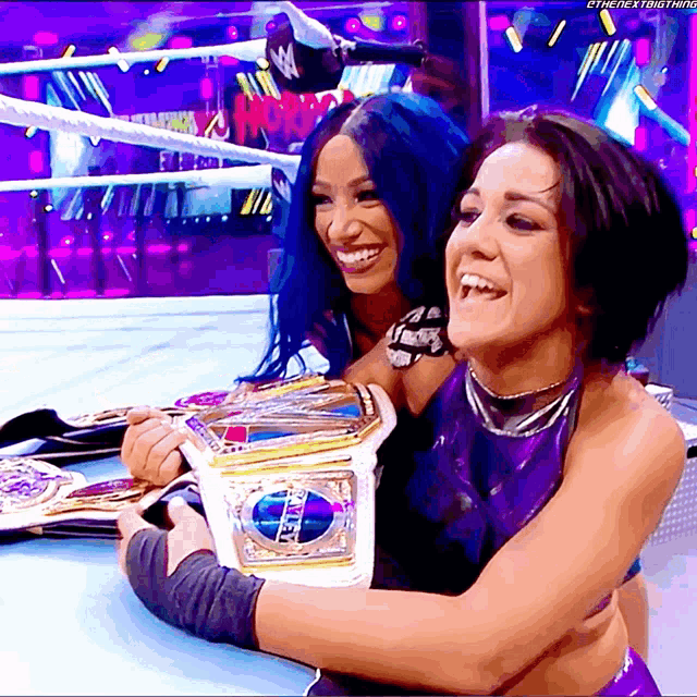 two female wrestlers are posing for a picture and one of them is holding a world heavyweight title