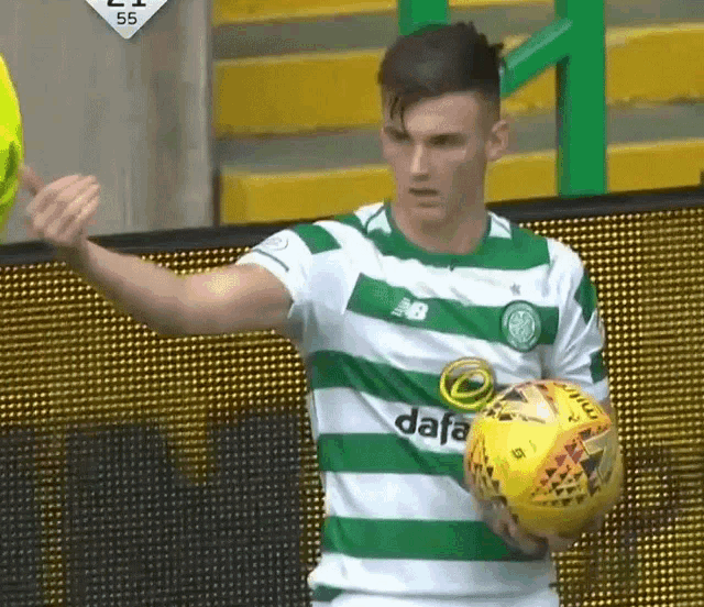 a soccer player wearing a green and white striped jersey is holding a yellow soccer ball .