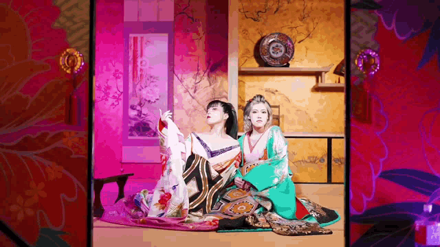 two women dressed in kimonos are sitting in a room