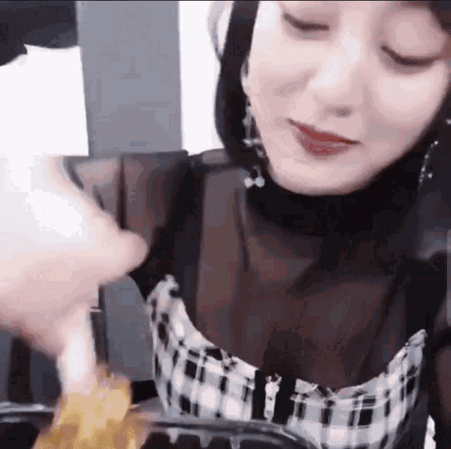 a woman in a plaid dress is eating food from a bowl with a fork .