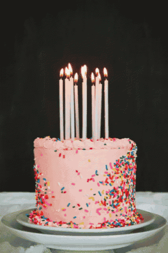 a birthday cake with pink frosting and sprinkles and lit candles