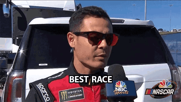 a man wearing sunglasses and a monster energy jacket talks into a microphone in front of a car