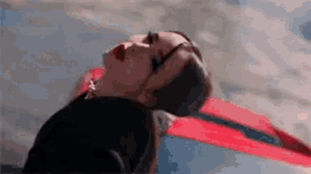 a woman is laying on the ground with her head on a red car hood .