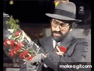 a man in a suit and hat is holding a bouquet of red roses
