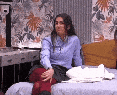 a woman in a blue shirt and red tights sits on a bed with her legs crossed