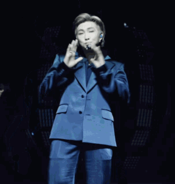 a man in a blue suit is standing on a stage with his hands up